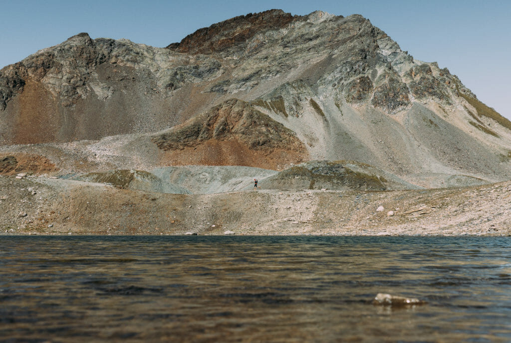 Tiny trail runner with lake at foreground and rocks in all different colours at the background